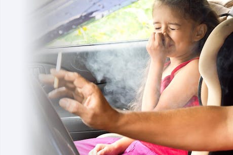 Child hold her nose because of secondhand smoke while her parent smokes in the car